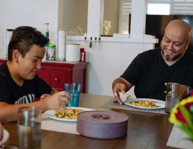 Latino man eating at a table with his son